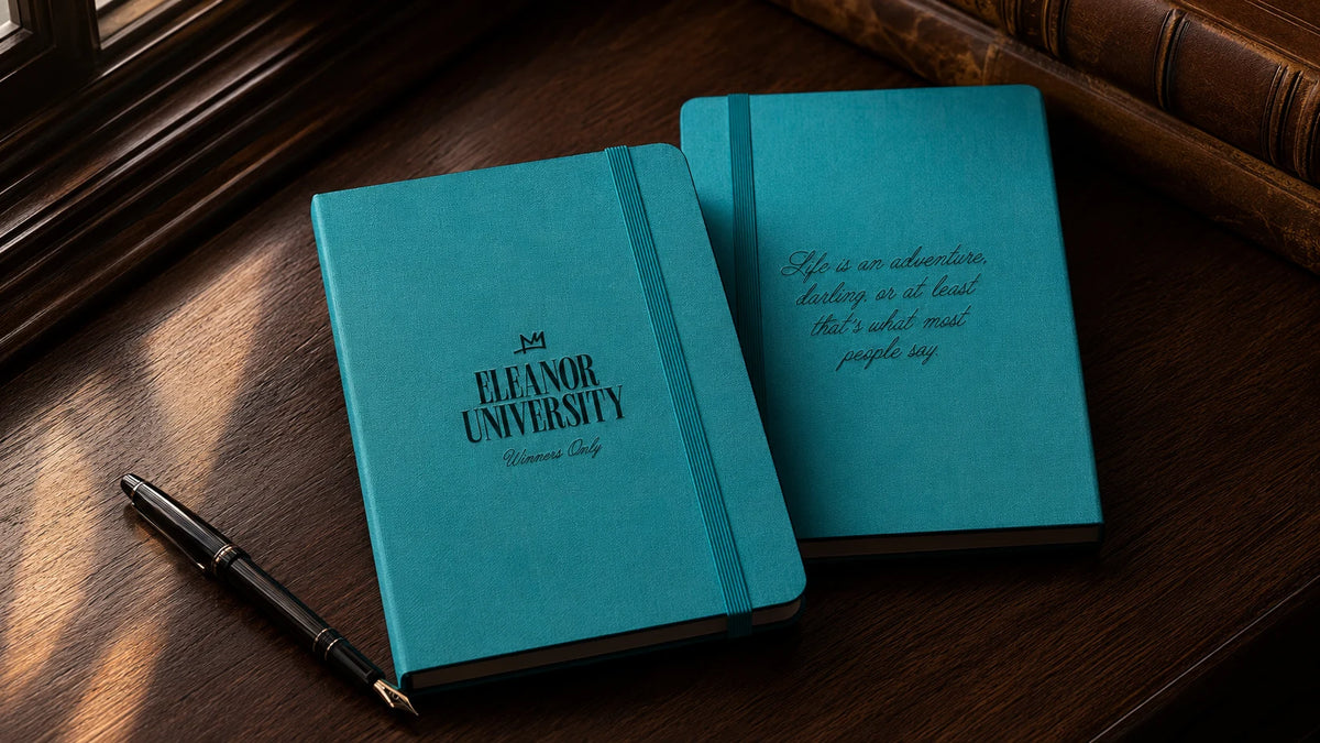 Turquoise Eleanor University notebooks on a wooden desk beside a pen