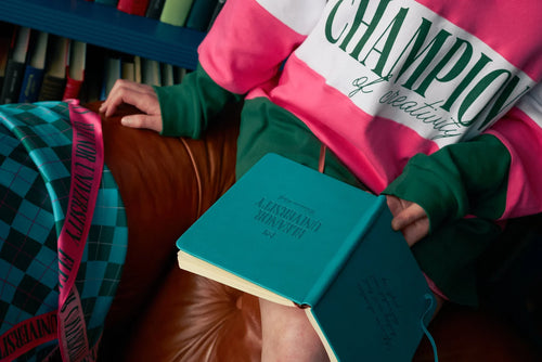 Face-free detail of the pink, white and forest-green Champions rugby shirt, worn with the University scarf and notebooks