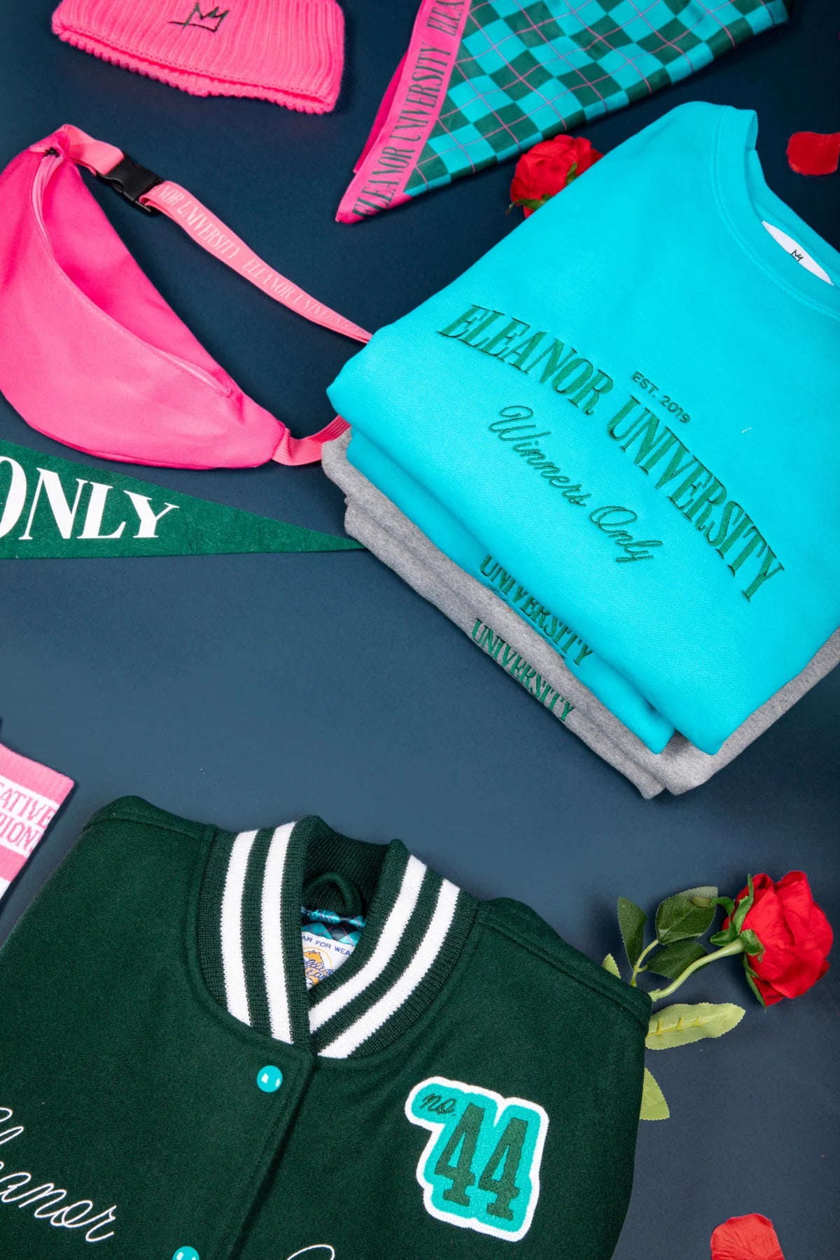 A turquoise Eleanor University sweatshirt folded above the grey colourway in a collection flatlay