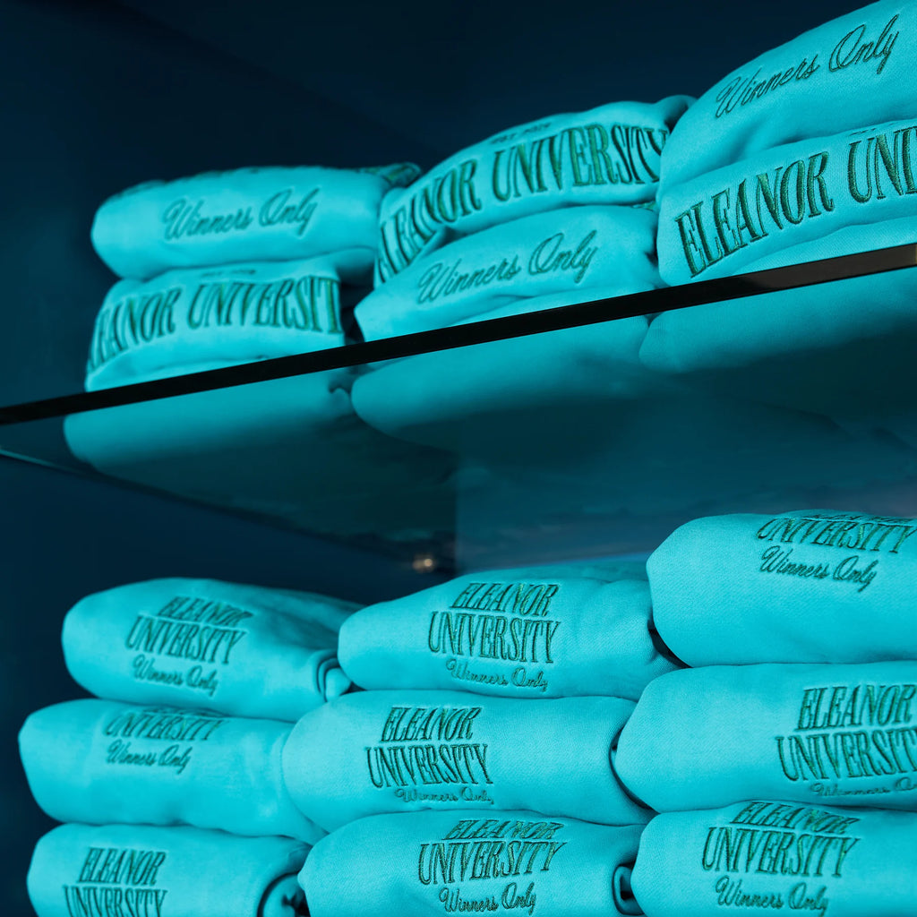Turquoise Eleanor University sweatpants folded on the lower shelves beneath matching sweatshirts